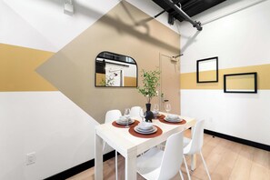 Un espace de salle à manger moderne avec une table dressée pour quatre personnes, des chaises blanches et une plante servant de décoration centrale.