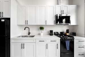 Une cuisine moderne avec des meubles blancs, un réfrigérateur noir, une hotte en acier inoxydable, une machine à café et une cuisinière.