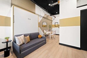 Ein modernes Interieur mit einem grauen Sofa, einem kleinen Tisch mit einer Pflanze und einem Essbereich mit weißen Stühlen und einem Tisch für vier Personen.