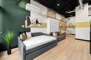 Ein modernes Interieur mit einem grauen Sofa, einem Essbereich und einer weißen Wand mit abstrakter Kunst.