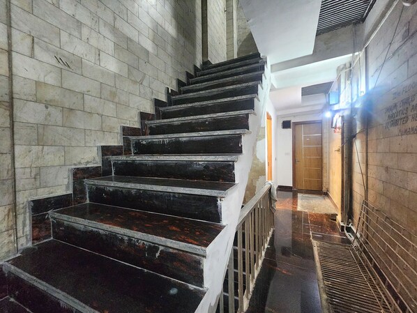 A staircase with a handrail, leading to a landing with a door. - Oly Hotel Yes Sir (New Delhi)