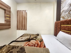 A small, single-bed room with a wooden headboard, a window with blinds, and a wall-mounted mirror. - Oly Hotel Yes Sir (New Delhi)