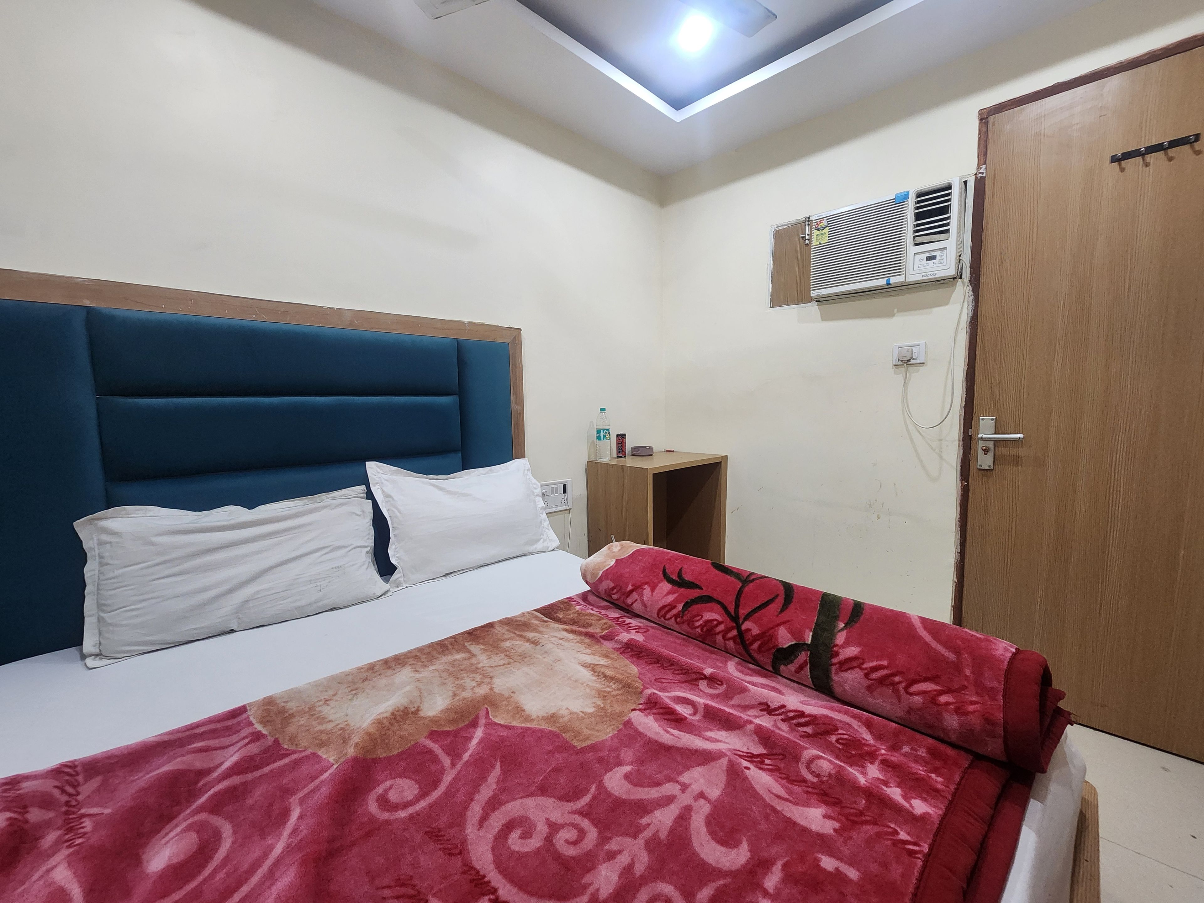 Een slaapkamer met een bed, een houten garderobe, een klein houten tafeltje en een airconditioning die aan de muur is bevestigd.