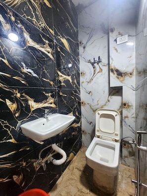 A bathroom with a black marble wall, a white sink, and a toilet. - Oly Hotel Yes Sir (New Delhi)