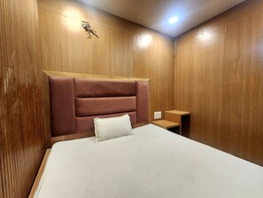 A room with a bed, wooden panel walls, a headboard, a bedside table, and a nightstand. - Oly Hotel Yes Sir (New Delhi)
