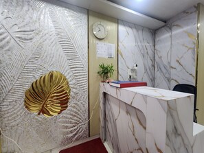 A reception desk with a clock, a plant, and a book on it. - Oly Hotel Yes Sir (New Delhi)