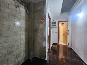 A corridor with tiled walls, a wooden floor, and a door leading to another room. - Oly Hotel Yes Sir (New Delhi)