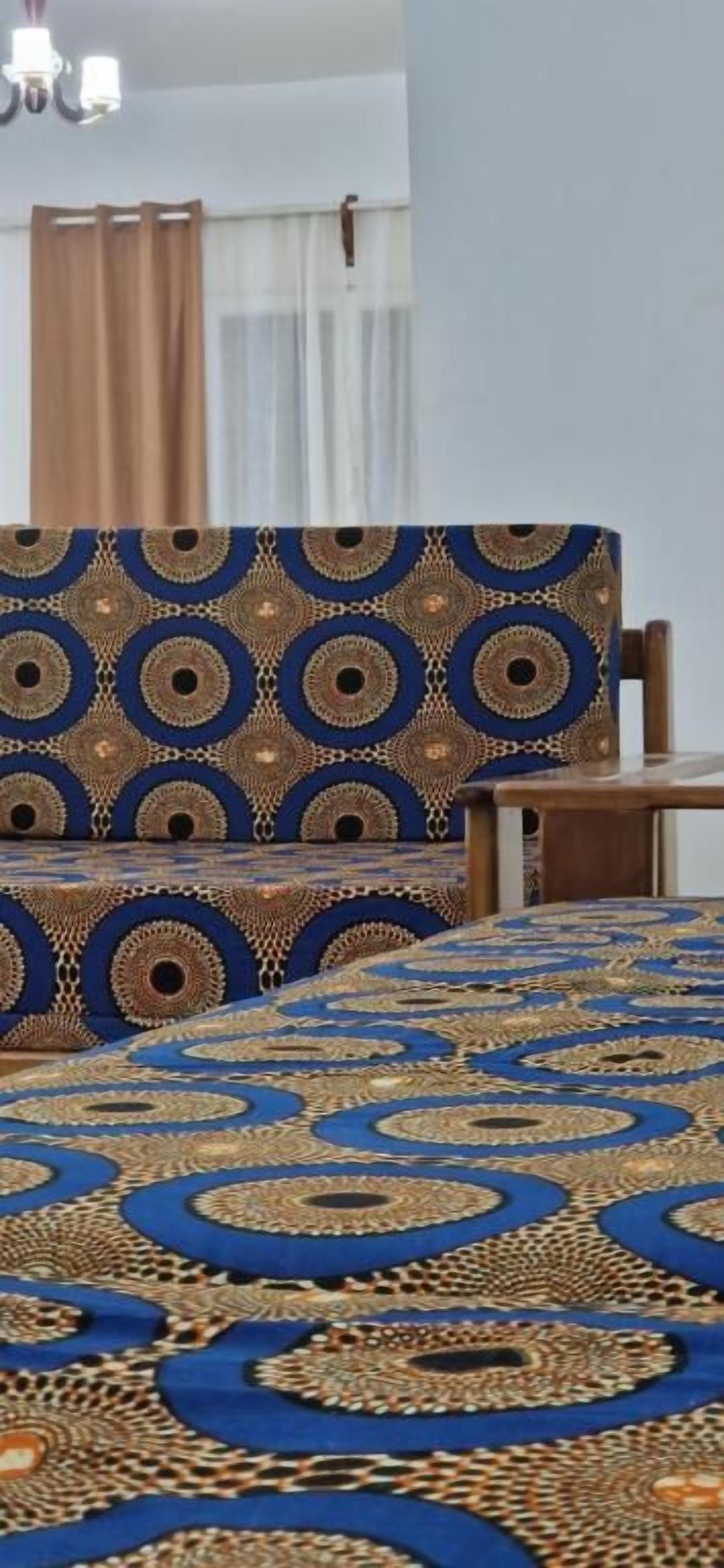 A room with a patterned bedspread, a wooden chair, and a window with curtains.