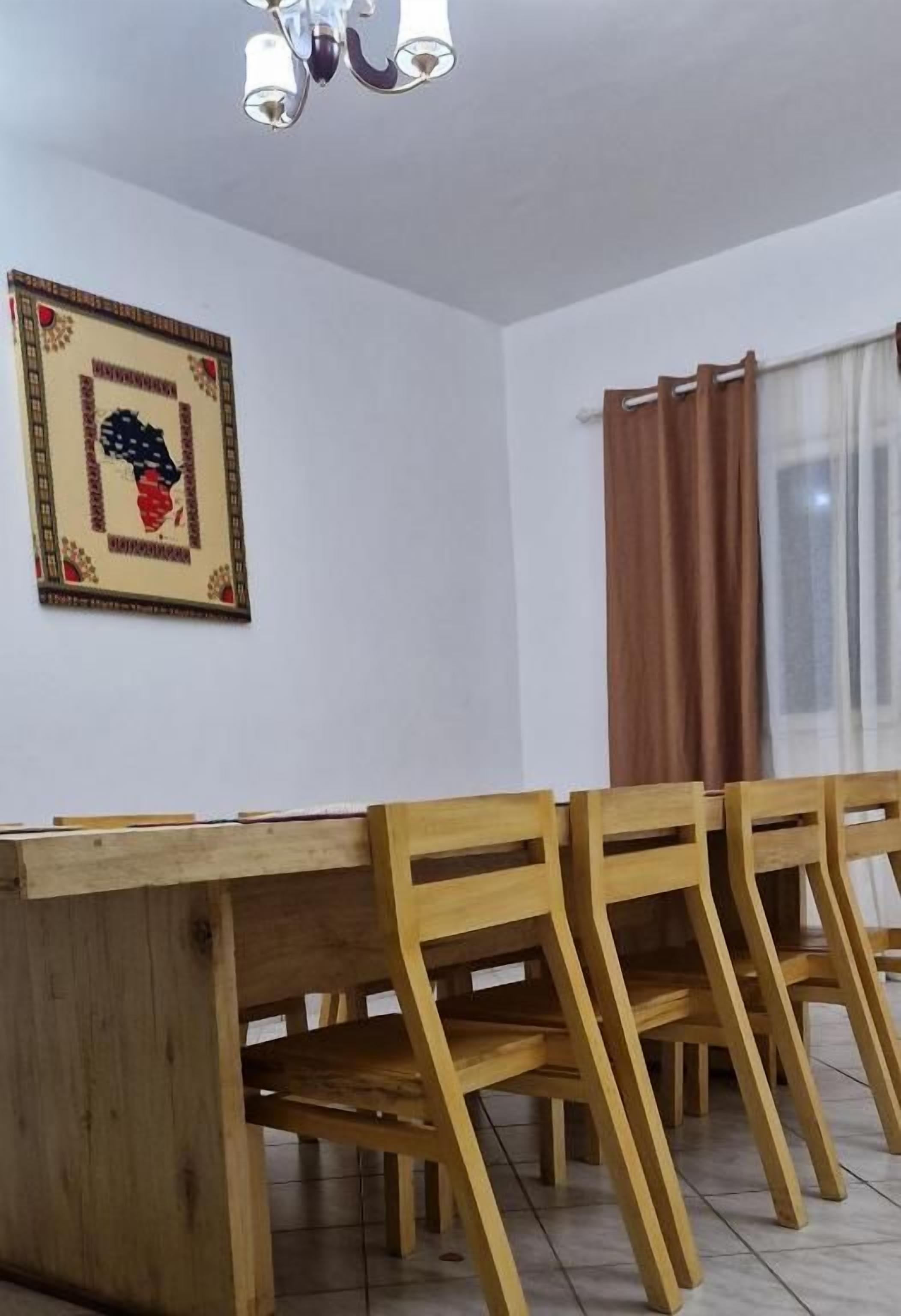 Et spiseområde med et træbord og stole, en loftlampe og et billede i ramme på væggen.