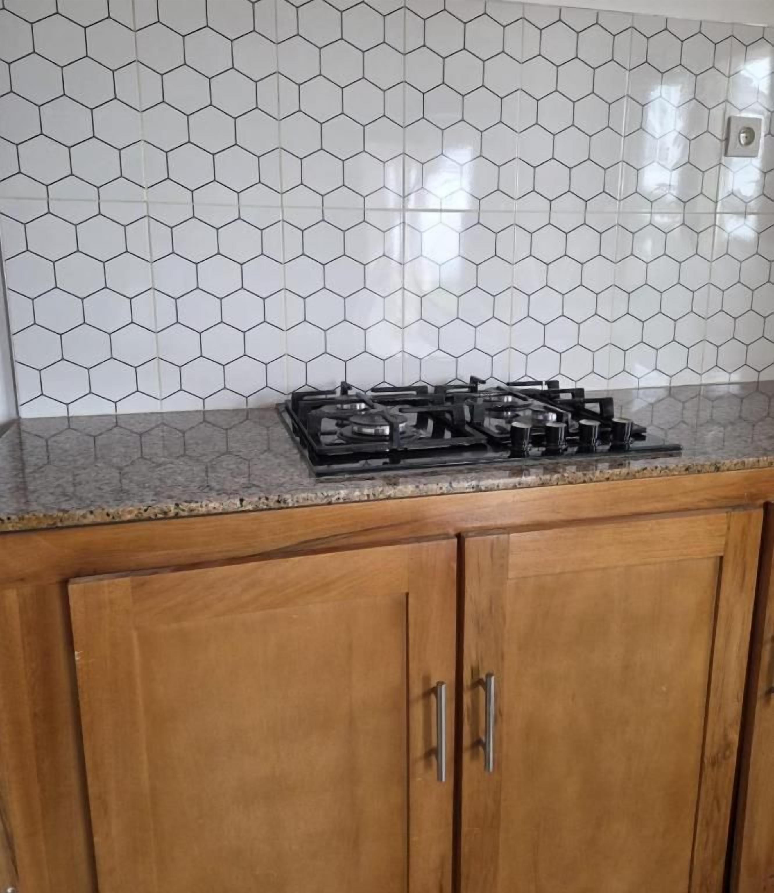 Et køkken med en backsplash af sekskantede fliser, en gasblus og træskabe.