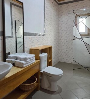 A bathroom with a wooden vanity, a white sink, a toilet, and a shower area. - SEED-Aeroport Nsimalen Yaounde (Yaounde)