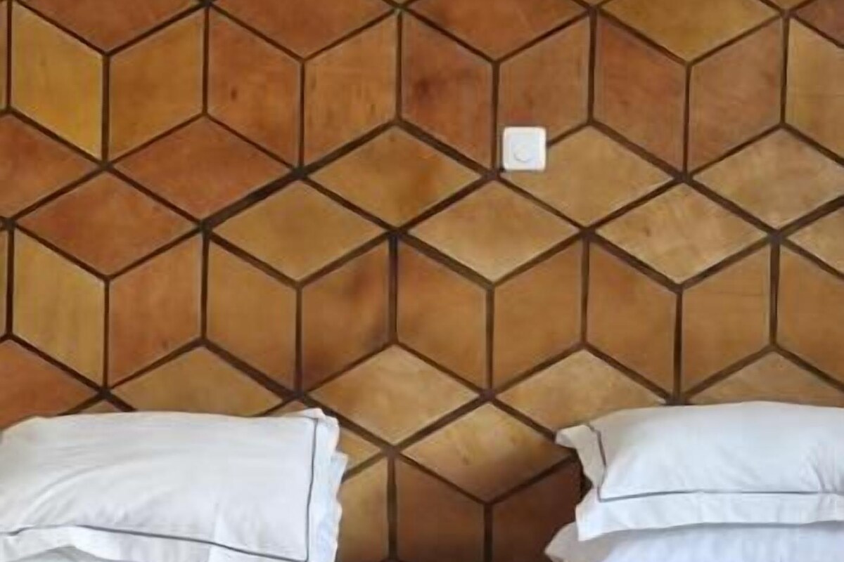 A bed with white bedding and pillows, a geometric patterned headboard, and a small white switch on the wall.