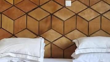Ein Bett mit weißer Bettwäsche und Kissen, ein Kopfteil mit geometrischem Muster und ein kleiner weißer Schalter an der Wand.