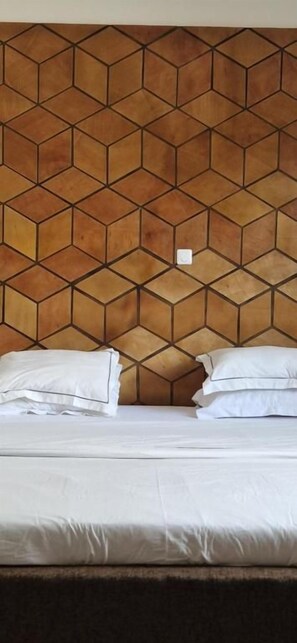 A bed with white bedding and pillows, a geometric patterned headboard, and a small white switch on the wall. - SEED-Aeroport Nsimalen Yaounde (NSIMALEN)