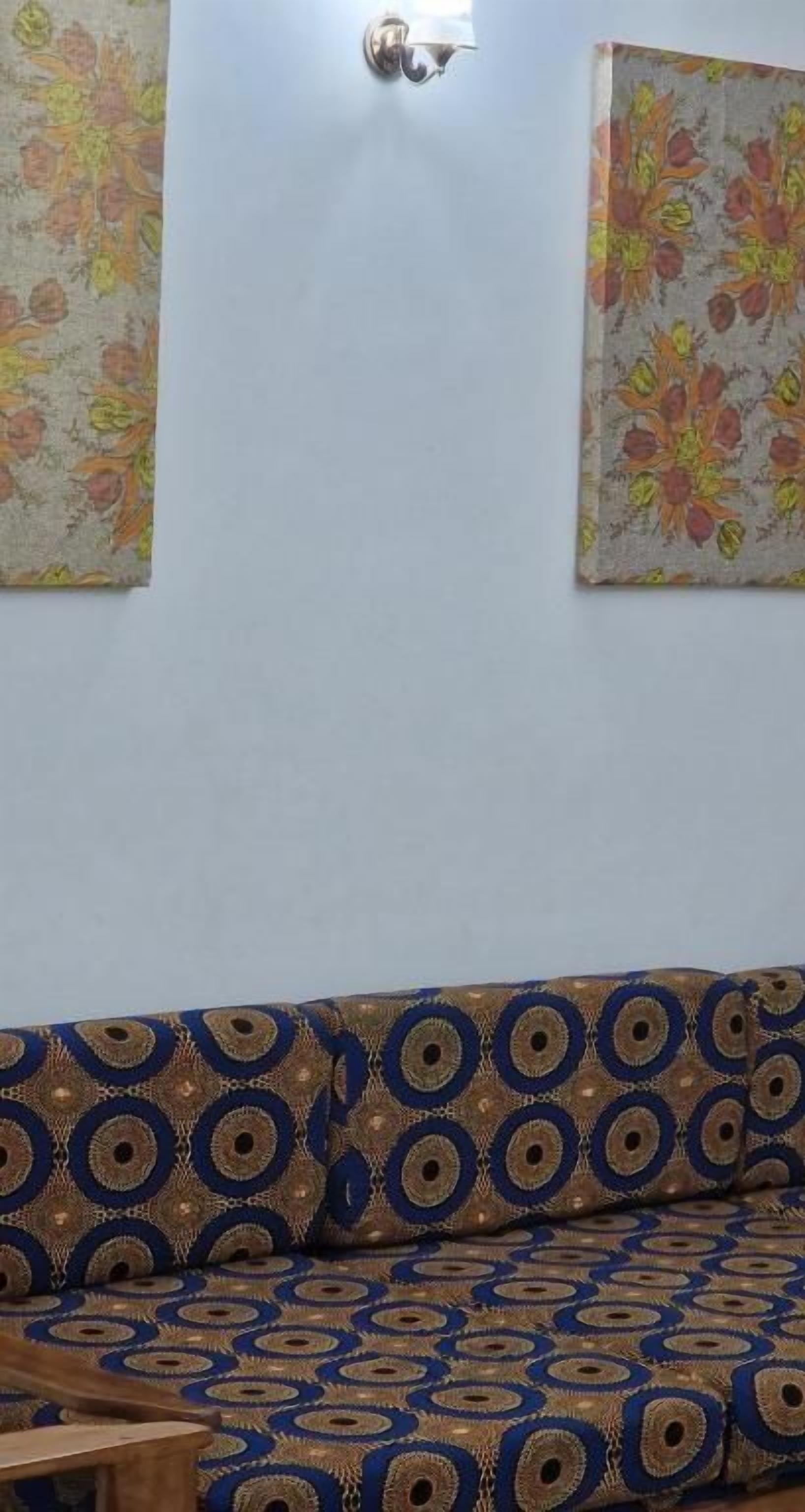 A room with a patterned sofa, a wall-mounted light fixture, and two floral wall decorations.