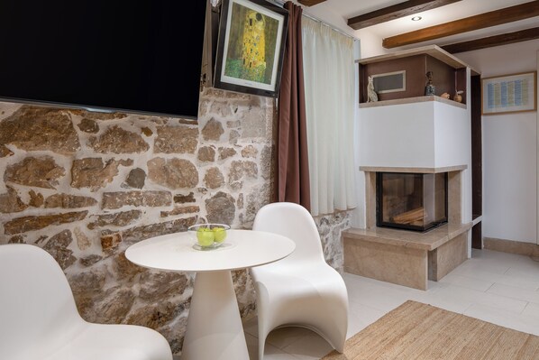 Una sala de estar acogedora con una pared de piedra, una chimenea, una mesa redonda blanca y dos sillas blancas.