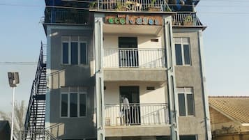 Un edificio de varios pisos con balcones, un automóvil estacionado adelante y una entrada protegida por un portón.