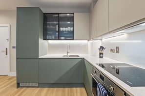 Une cuisine moderne dotée d’un four encastré, d’un évier en acier inoxydable et d’une fenêtre avec des stores.