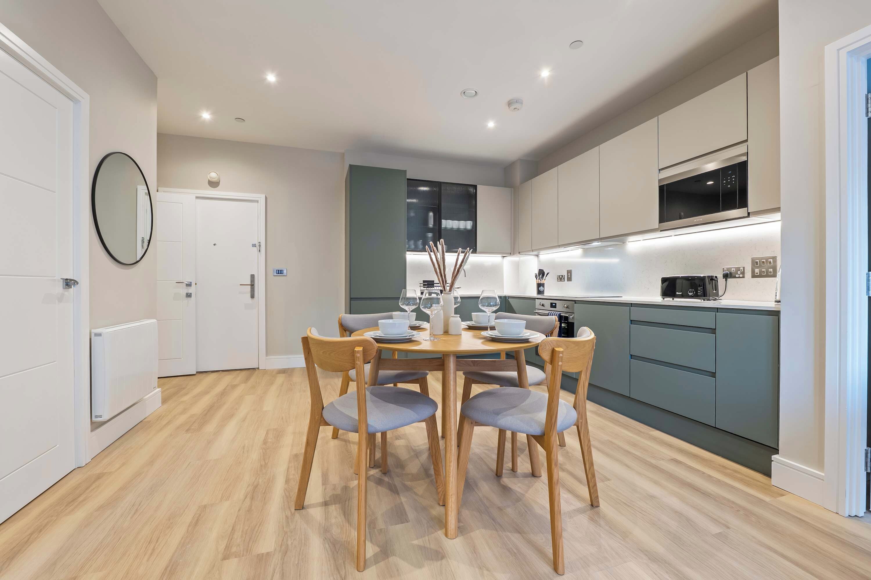 A modern kitchen with a dining area, wooden chairs, and a round table.