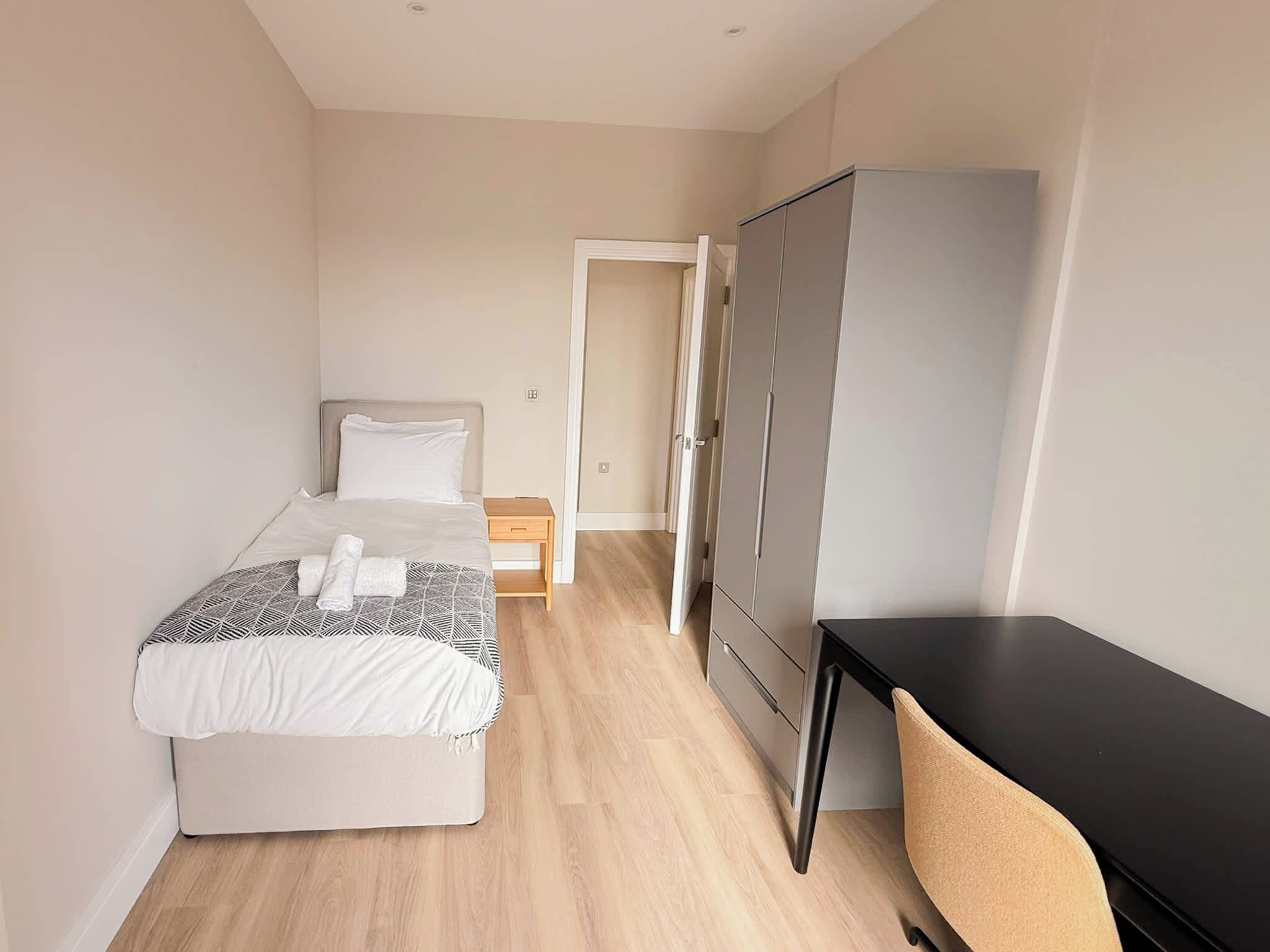 A hotel room with a bed, a desk, a wardrobe, and a door leading to another room.