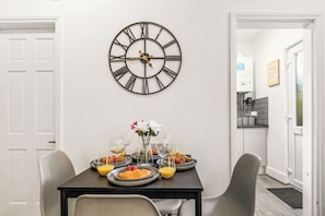 A dining area with a wall-mounted clock, a table set with plates, glasses, and a vase with flowers. - Luxury Garden Apartment 2Bed 2Bath Nottingham (Nottingham)
