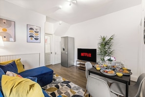 Moderni olohuone, jossa on sohva, sohvapöytä, televisio, jossa näkyy Netflix, sekä ruokailutila aamiaistarvikkeineen.