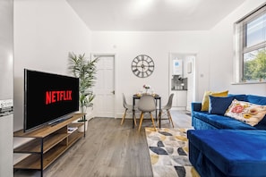 A modern living room with a flat-screen TV, a dining area, and a blue sofa. - Luxury Garden Apartment 2Bed 2Bath Nottingham (Nottingham)