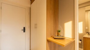 A room with a door, a wooden shelf with a plant, and a bathroom visible in the background. - Studio com Piscina a 400m do Metr Eucaliptos (São Paulo)