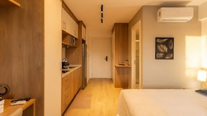 A hotel room with a bed, a desk, a kitchenette, and a door leading to another room. - Studio com Piscina a 400m do Metr Eucaliptos (São Paulo)