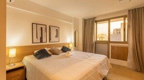 Habitación de hotel con cama, mesita de noche, lámpara y una ventana con cortinas.