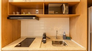 A compact kitchen with a built-in microwave, a stove, a sink, and a water dispenser. - Studio com Piscina a 400m do Metr Eucaliptos (São Paulo)