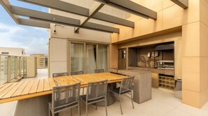 A rooftop terrace with a wooden dining table and chairs, a grill, and a view of the cityscape. - Studio com Piscina a 400m do Metr Eucaliptos (São Paulo)