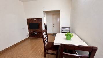A room with a dining table, chairs, a TV on a wooden stand, and a potted plant on the table.