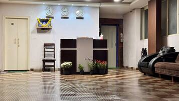 A hotel lobby with a reception desk, clocks, a sofa, and a chair.
