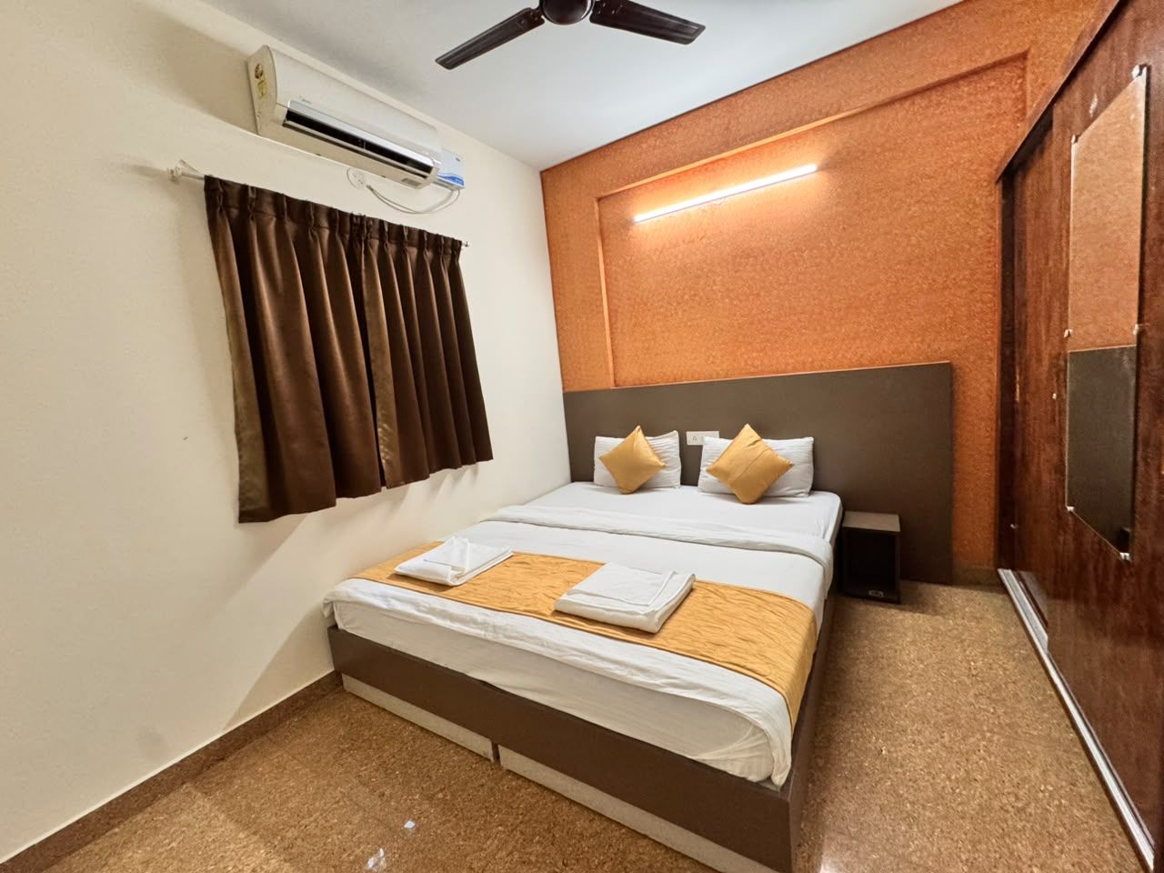 Habitación de hotel con una cama, ventilador de techo, aire acondicionado, televisor y ventana con cortinas.