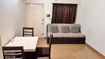 Una habitación con una mesa de comedor, sillas, un sofá con cojines estampados, una puerta y una ventana con cortinas.