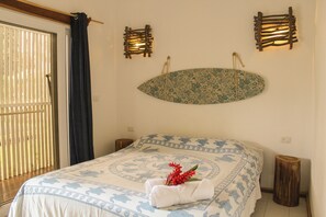 Una cama bien hecha con una colcha estampada, un adorno en la pared y un taburete de madera.