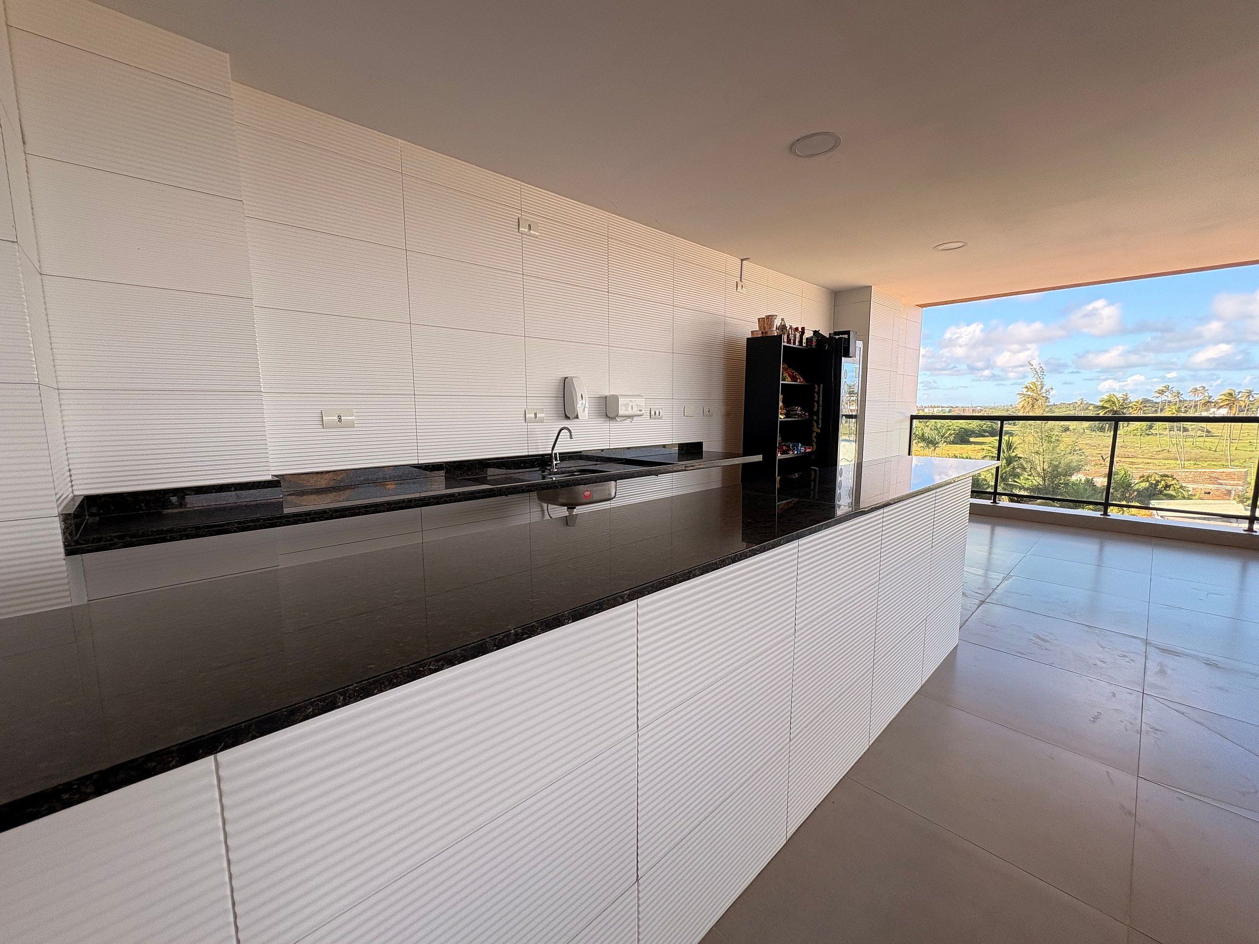Cocina moderna con encimera negra, salpicadero de azulejos blancos y vistas al campo desde un balcón.