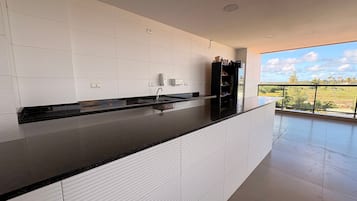 Cocina moderna con encimera negra, salpicadero de azulejos blancos y vistas al campo desde un balcón.