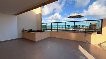Un balcon spacieux offrant une vue dégagée sur la plage et l’océan, agrémenté d’une balustrade en verre, de mobilier d’extérieur et d’une plante en pot.
