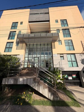Un edificio de varios pisos con una entrada central, una escalera y un acceso con portón.