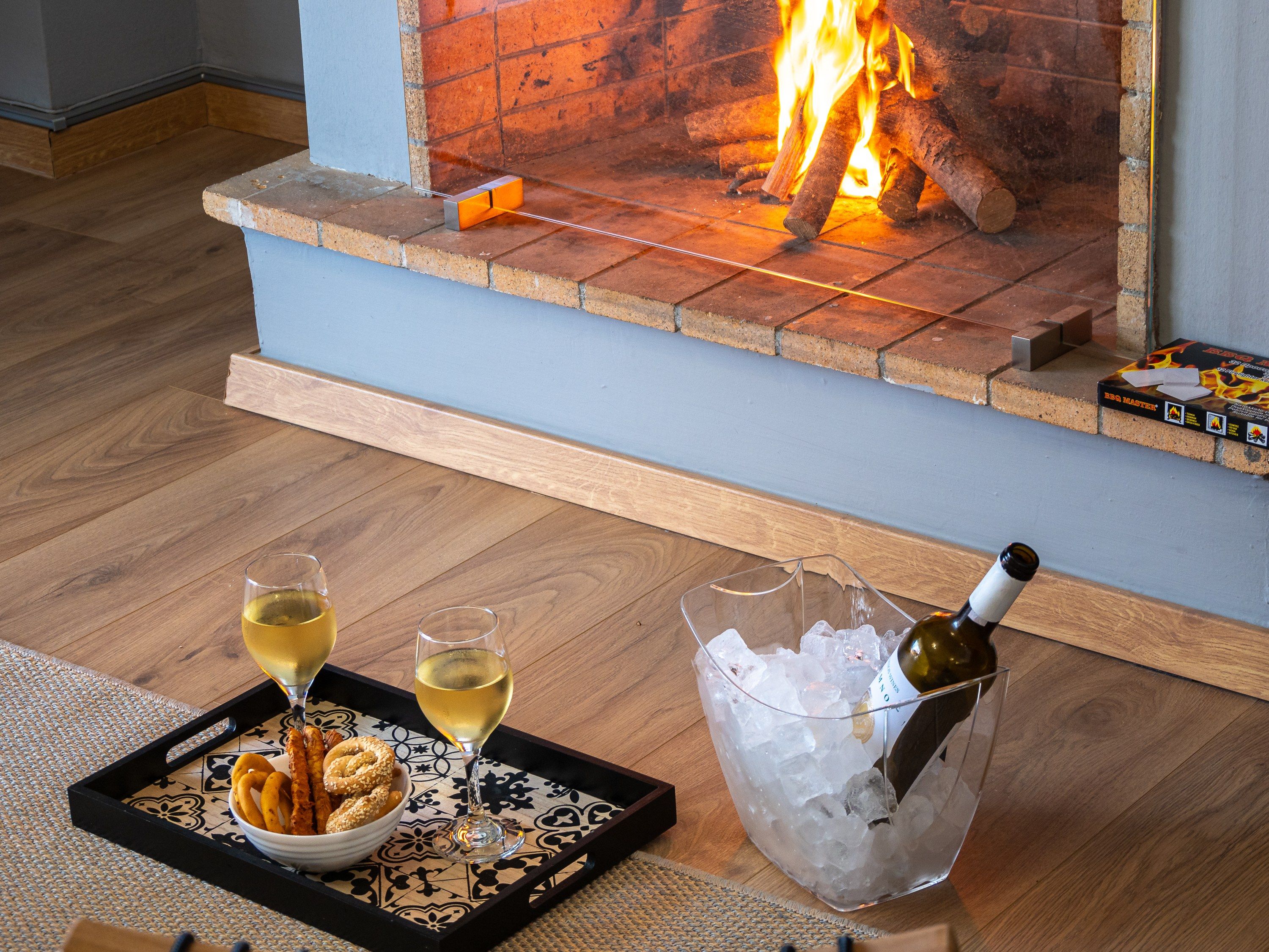 En öppen spis med ved, ett fat med kringlor och glas med vin, och en flaska champagne i en hink.