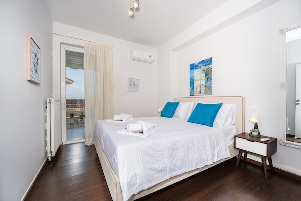 A hotel room with a bed, a nightstand, a mirror, a window with curtains, and a wall with a painting.