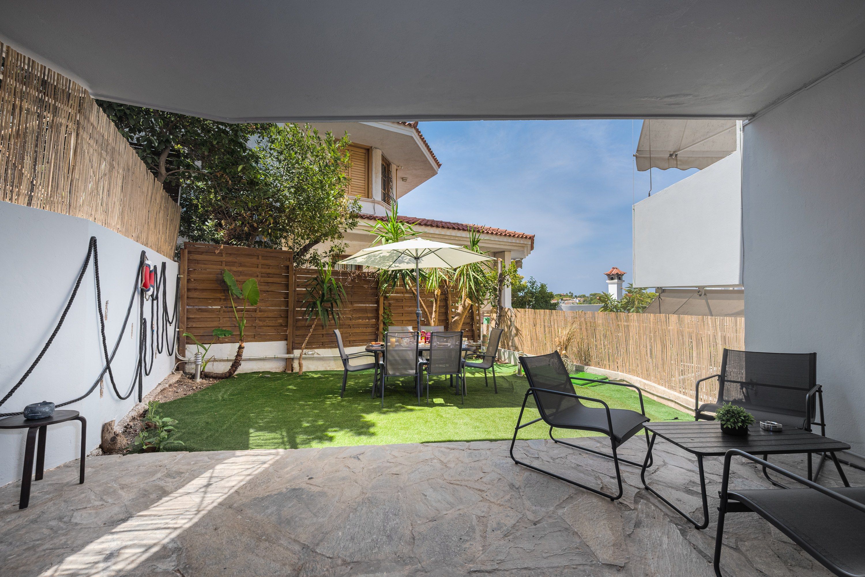 Un patio con mesa y sillas, un jardín pequeño con césped artificial y una valla de madera.