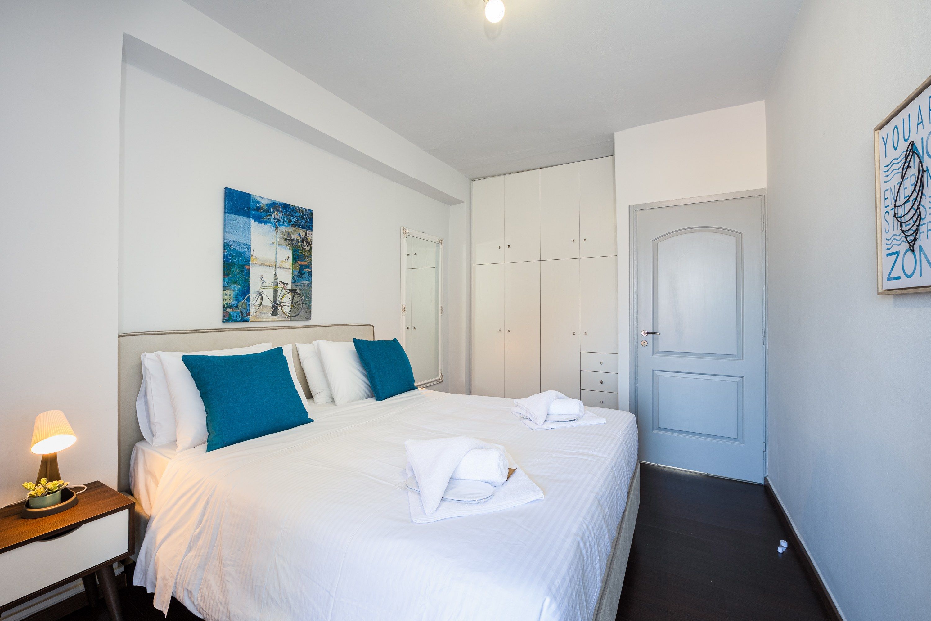 Habitación de hotel con cama, mesita de noche, lámpara, obra de arte, armario y puerta.