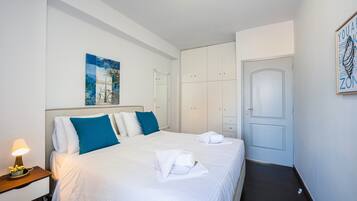 A hotel room with a bed, bedside table, lamp, artwork, wardrobe, and a door.