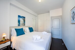 A hotel room with a bed, bedside table, lamp, artwork, wardrobe, and a door.