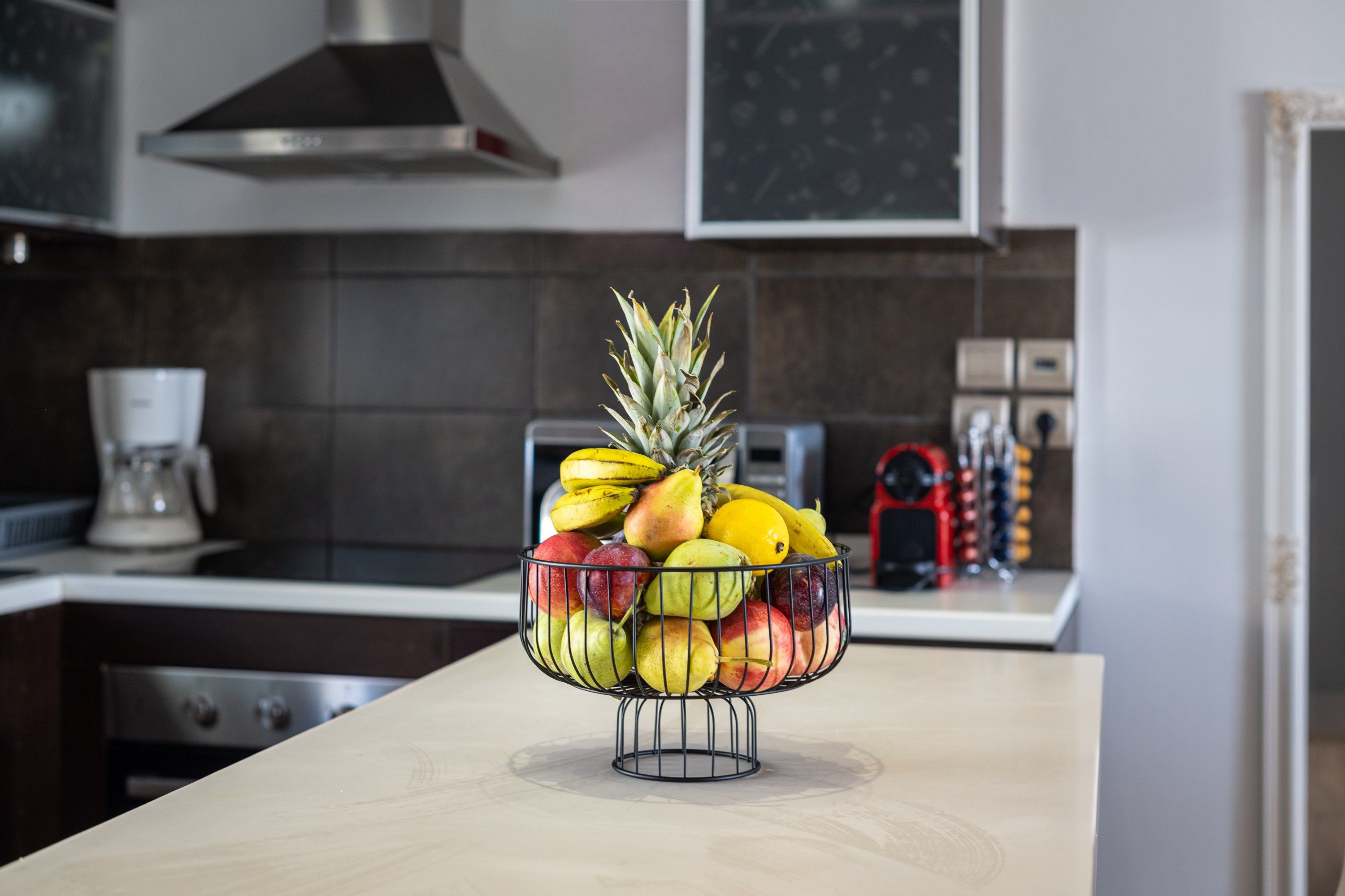 Una encimera de cocina con un frutero que contiene manzanas, peras, plátanos y una piña.
