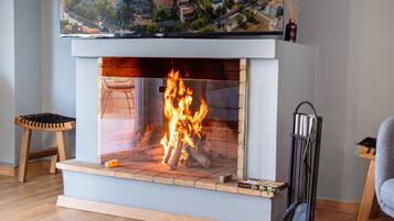Una chimenea moderna con frente de vidrio transparente, un taburete de madera y un adorno en la repisa.