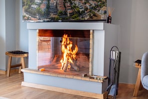 A modern fireplace with a clear glass front, a wooden stool, and a decorative item on the mantel.